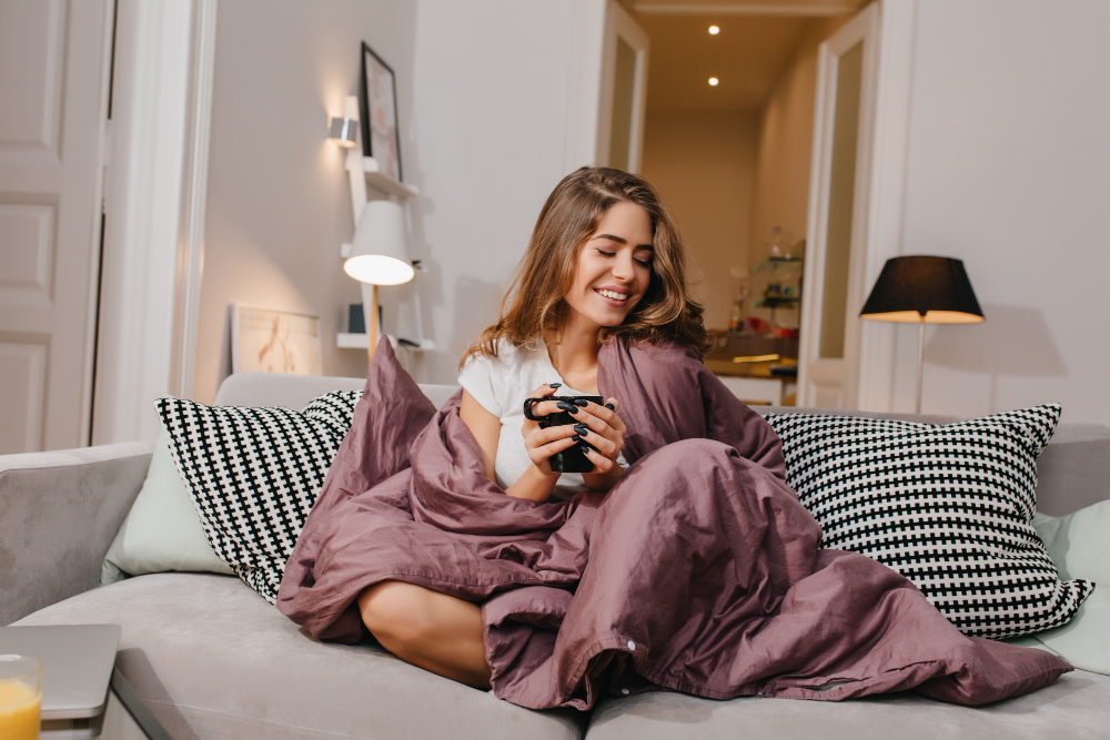 cheerful woman sitting couch with blanket cushions smiling